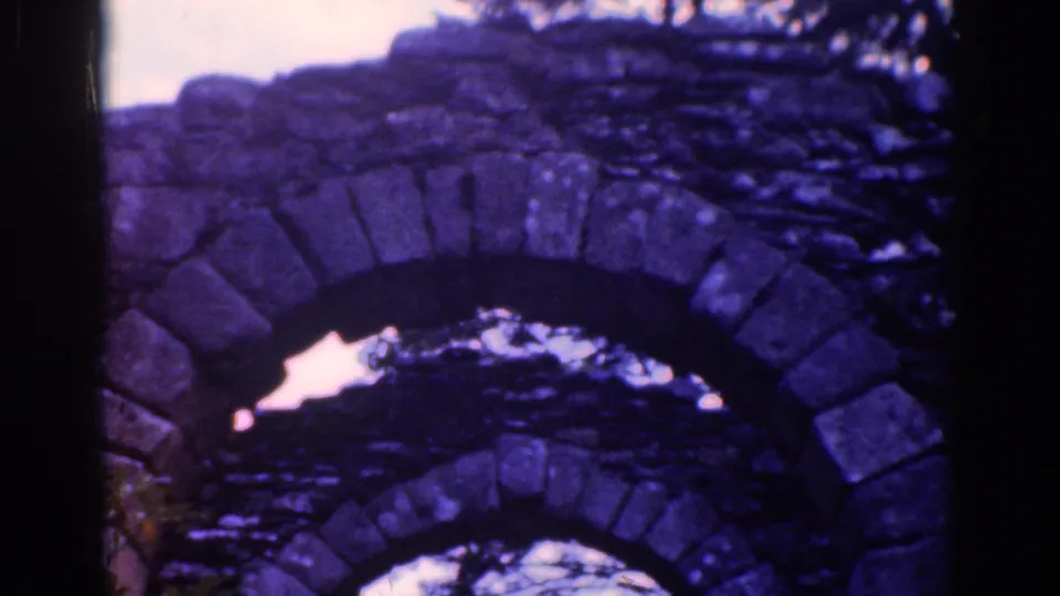 Close 8mm view of stacked weathered stone arches, likely on the historic estate grounds, with branches and sky visible beyond.