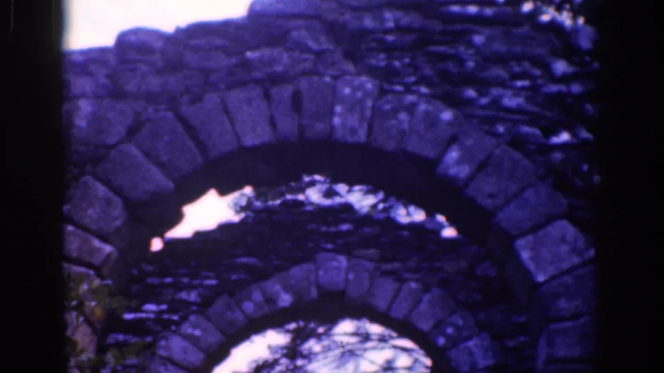 Final frame holds on layered weathered stone arches, with tree branches and pale sky showing through the lower opening.