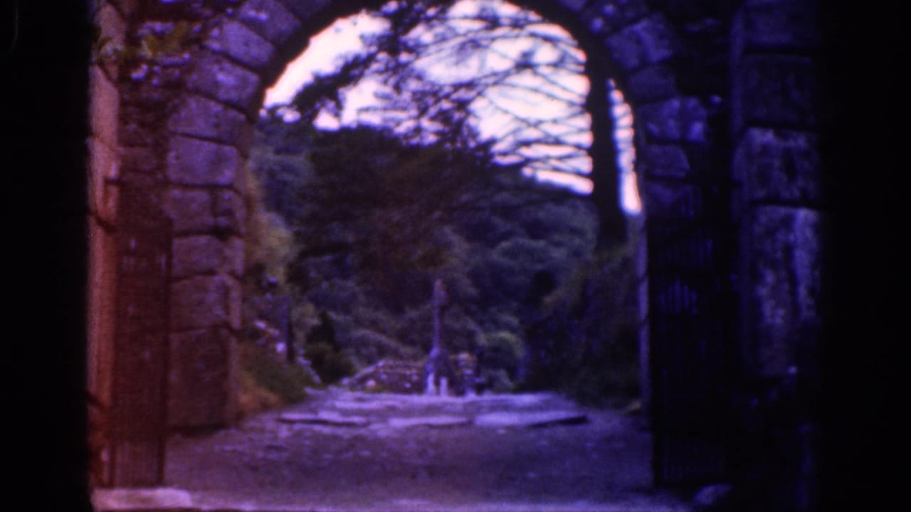 Stone archway framing a wooded path with an iron gate at the side.