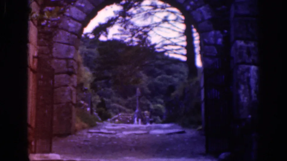 1961 8mm Ireland footage showing a stone archway, dark iron gate, bare branches, and a wooded path beyond.