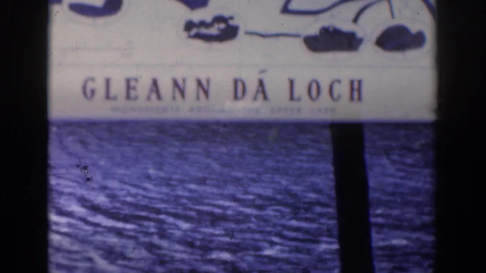 1961 8mm frame showing the Gleann Da Loch sign over rippled lake water, partly blocked by a dark tree trunk.