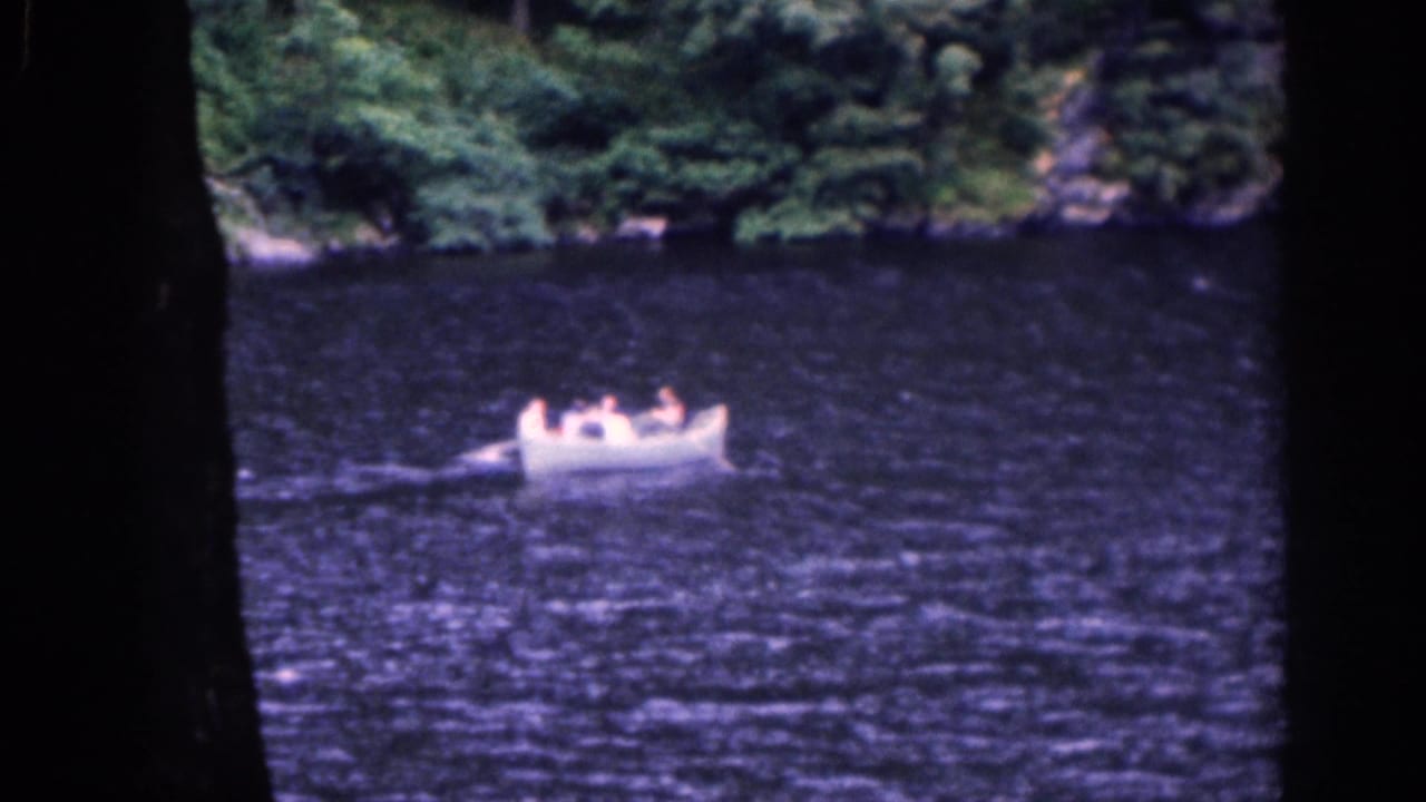 White rowboat on rippled lake water with people aboard and trees along the far bank.