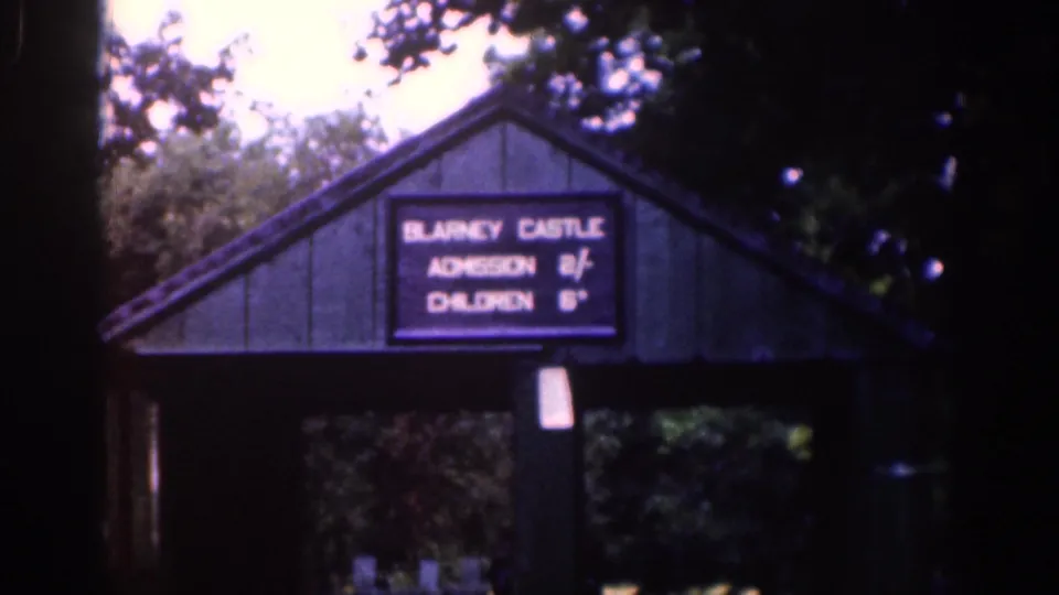 1961 Ireland travel frame showing a Blarney Castle admission sign on a small entrance structure under trees.