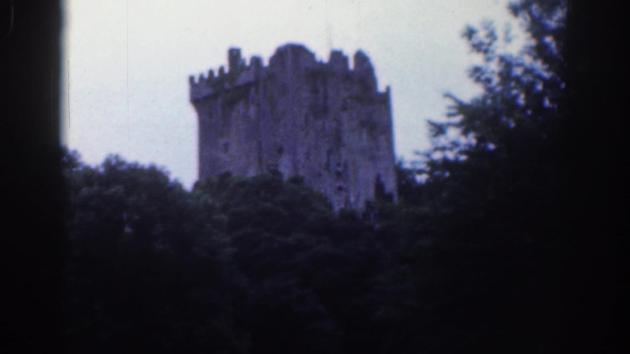 Distant 1961 home-movie view of Blarney Castle's stone tower above dense greenery, with soft focus and dark frame edges.