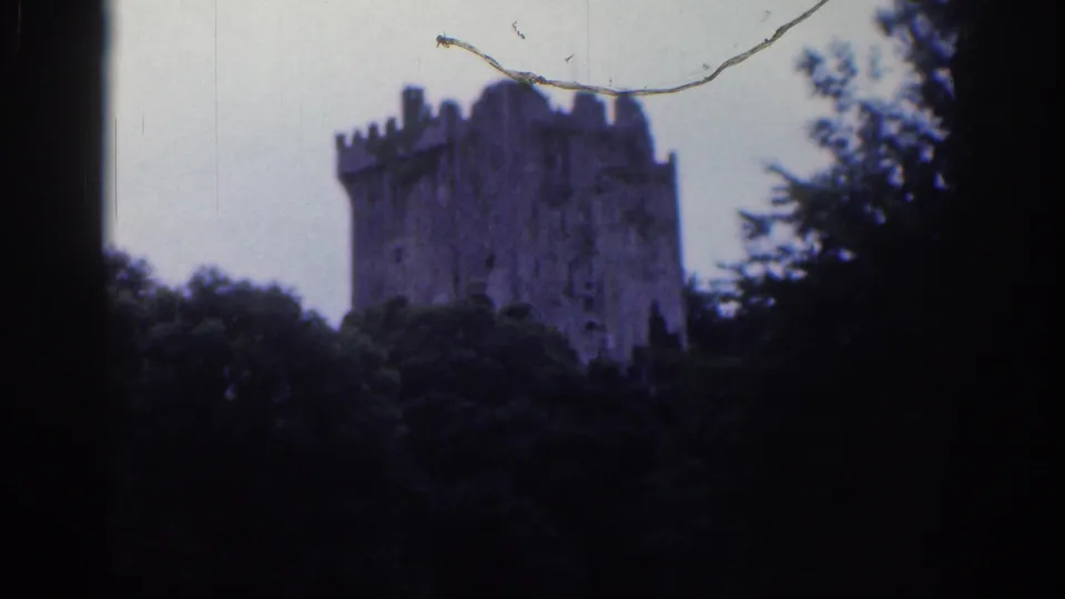 Distant view of Blarney Castle tower in 1961 8mm footage, with foliage at the sides, pale sky, and visible film wear.