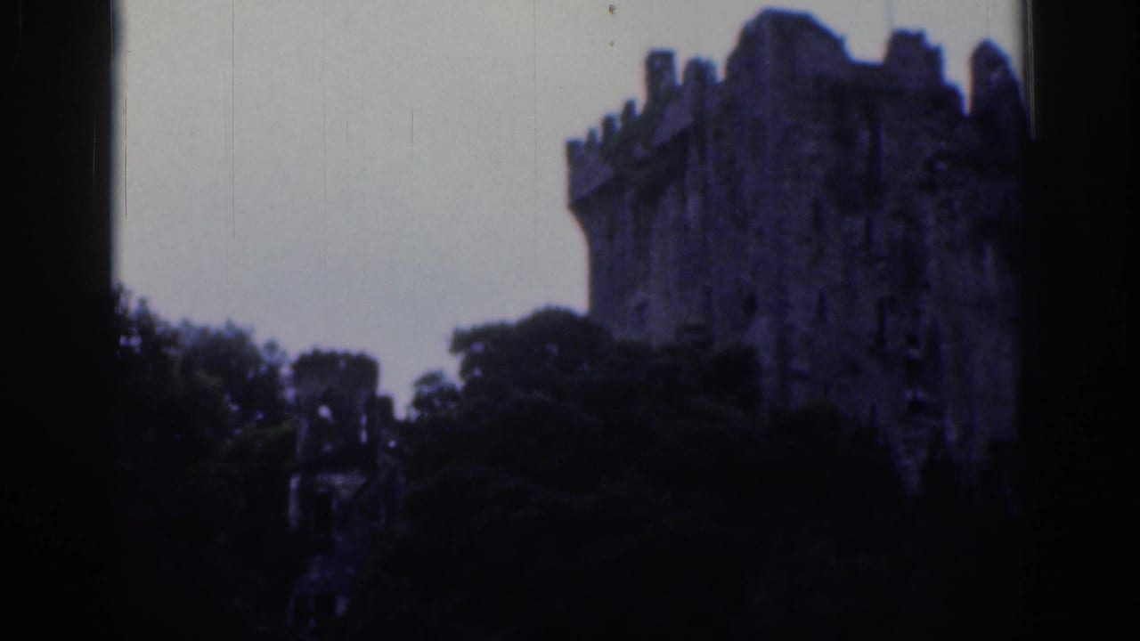 1961 Dublin home-movie still with a crenellated castle tower partially obscured by trees and darkened by the film exposure.