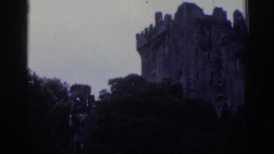1961 Dublin home-movie still with a crenellated castle tower partially obscured by trees and darkened by the film exposure.