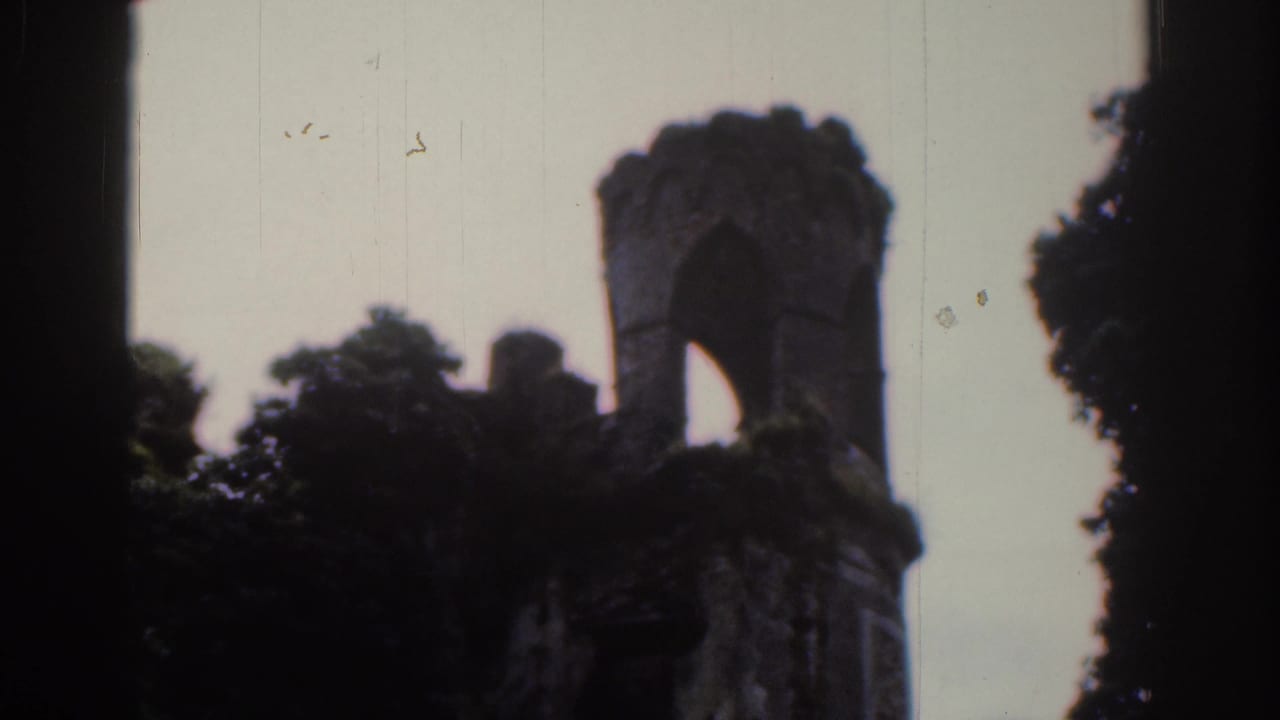 1961 Dublin 8mm frame of a ruined stone turret with a tall arch, dark trees and visible aged-film texture.