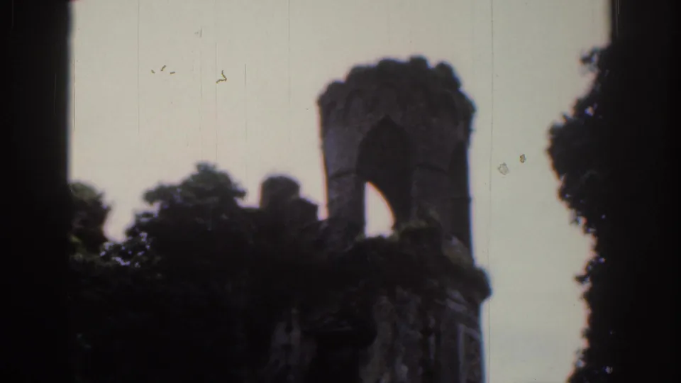 1961 Dublin 8mm frame of a ruined stone turret with a tall arch, dark trees and visible aged-film texture.