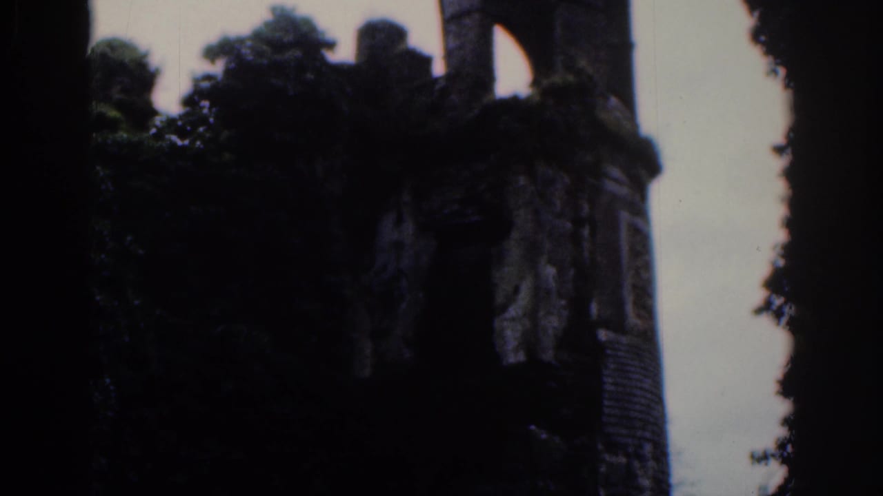 1961 Dublin home-movie frame showing weathered castle ruins and dense trees against a cloudy sky.