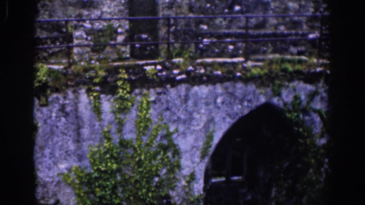 A rain-darkened castle wall in Dublin shows moss, railings, and a shadowed arched opening in vintage 8mm footage.