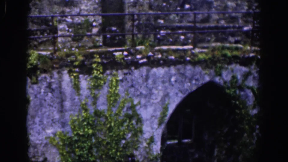 A rain-darkened castle wall in Dublin shows moss, railings, and a shadowed arched opening in vintage 8mm footage.