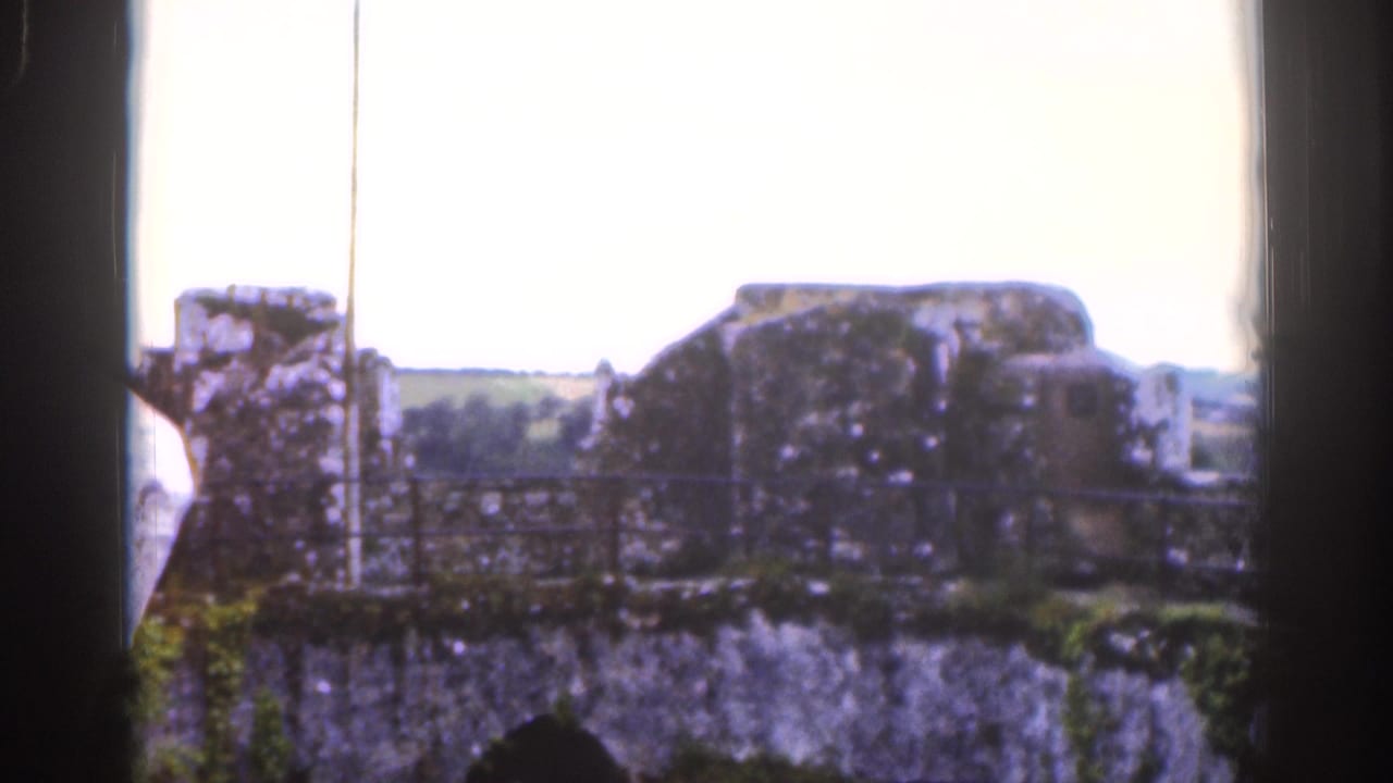 1961 Dublin home-movie frame showing old stonework and distant fields through dark framing, with soft focus and faded color.