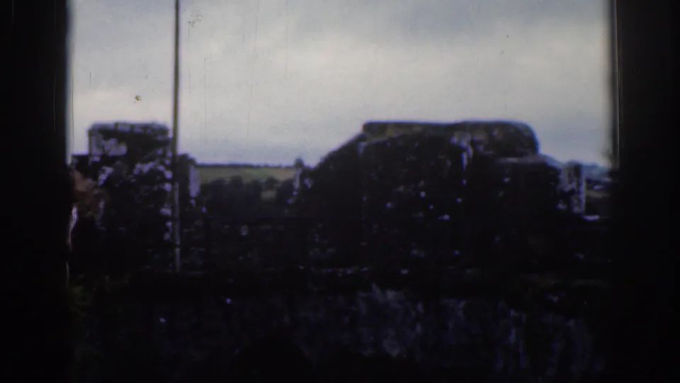 Dublin 1961 8mm frame with weathered stonework silhouetted against a pale sky and distant green fields.