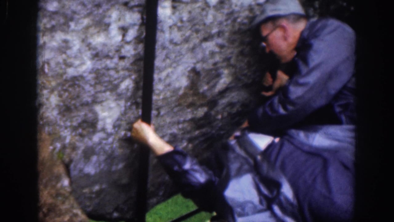 The visitor remains braced beside the stone wall, with a helper partly visible as he leans into position.