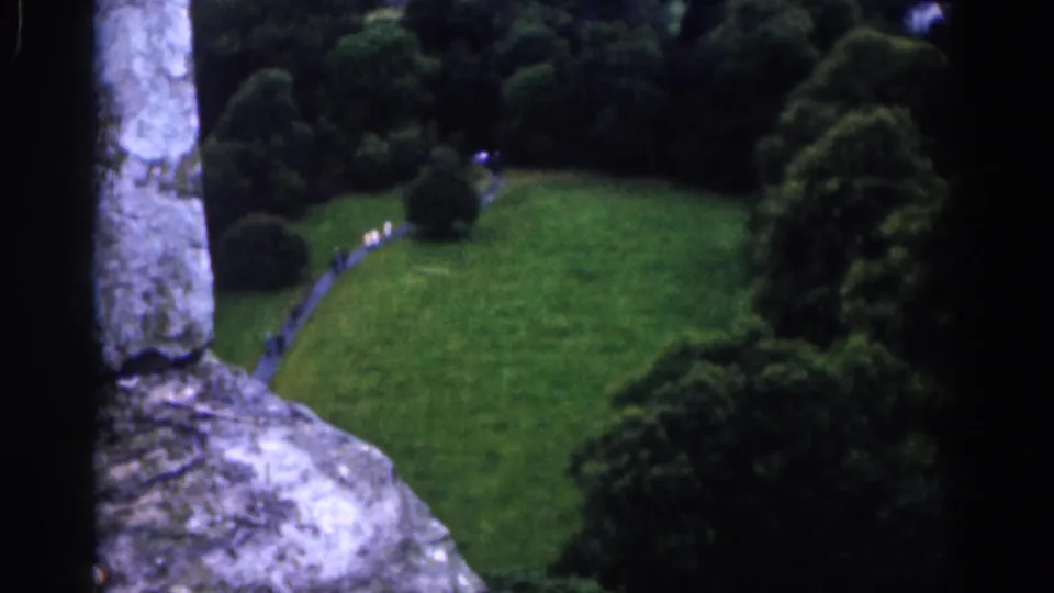 1961 Dublin castle lookout view over a green garden with a curving path, trees, and small pedestrians in the distance.