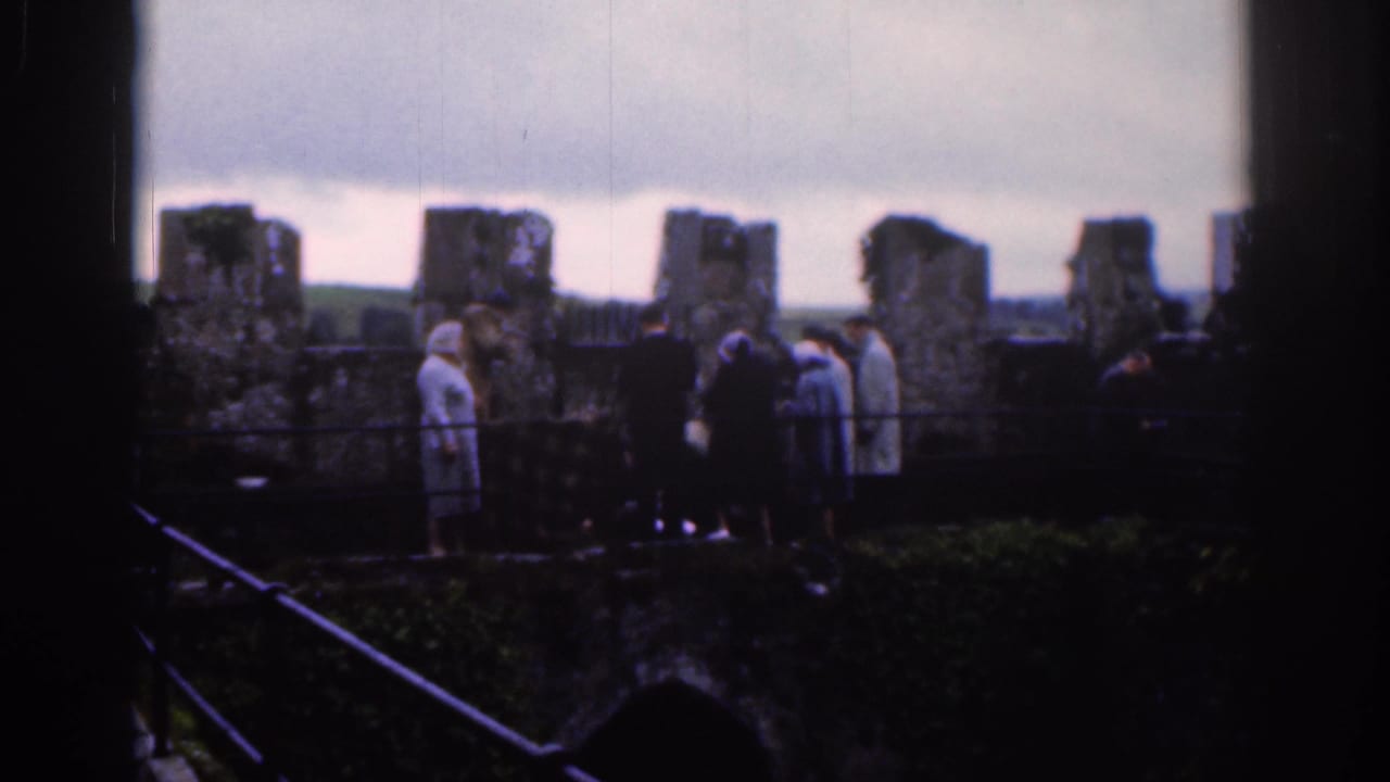 1961 Dublin home-movie frame showing visitors near old stone ruins, seen through dark foreground framing.