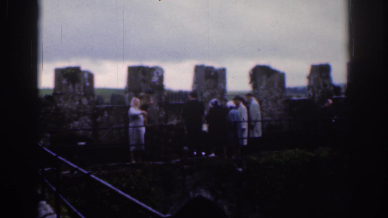 Small group of visitors stands along a railing in front of old stone wall sections.