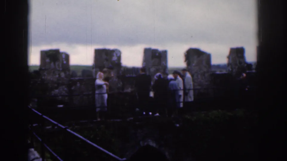 Tourists at a Dublin ruins site in 1961, with weathered stonework and distant landscape beyond the wall.