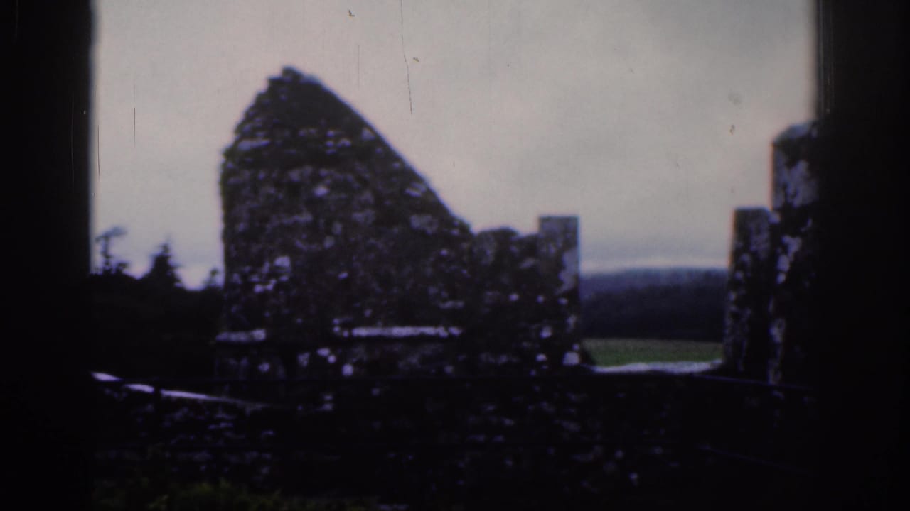1961 Dublin 8mm frame looking across a broken stone wall, ruined battlements, and distant green landscape.