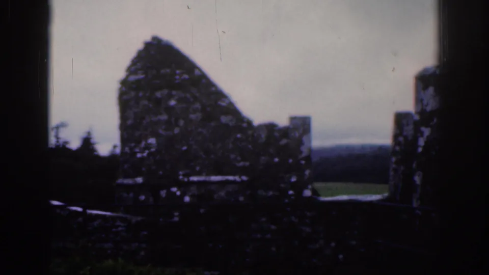 1961 Dublin 8mm frame looking across a broken stone wall, ruined battlements, and distant green landscape.