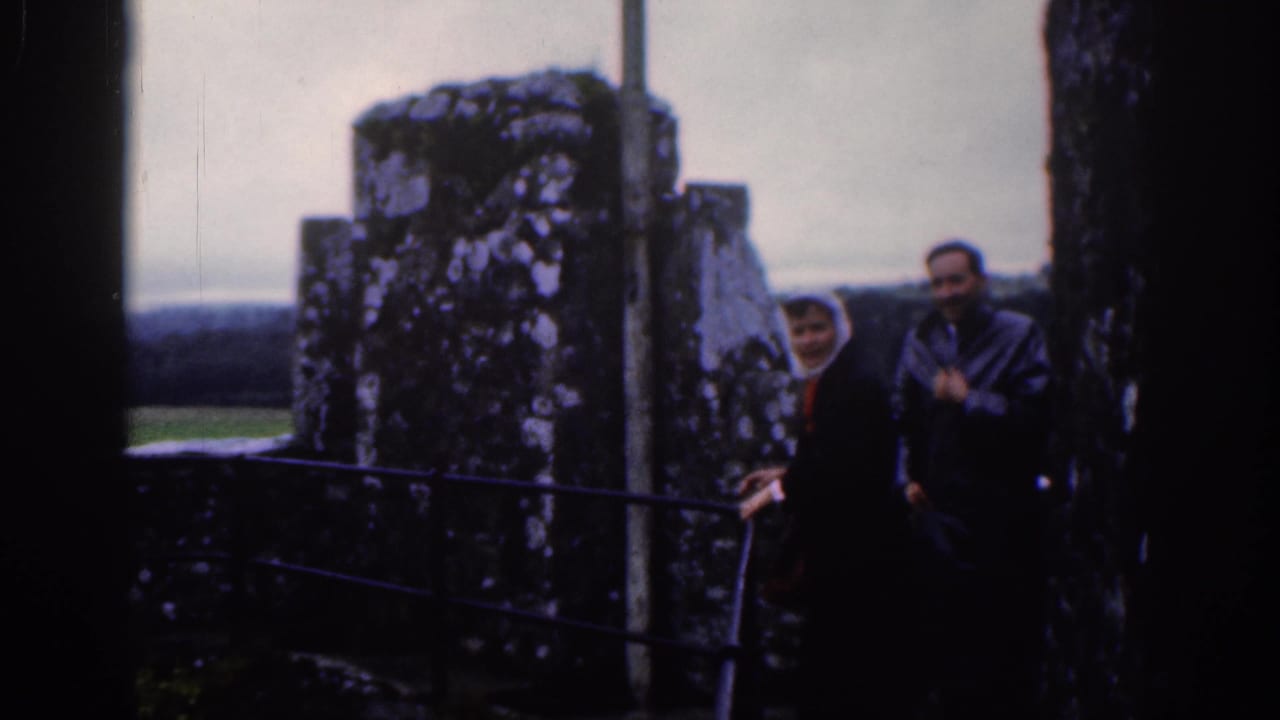 A woman in a white headscarf and a man stand beside stone ruins and railings.