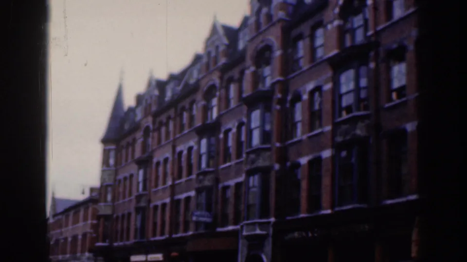 1961 Dublin 8mm frame showing a row of red-brick townhouses with bay windows, gabled rooflines, and a distant spire.