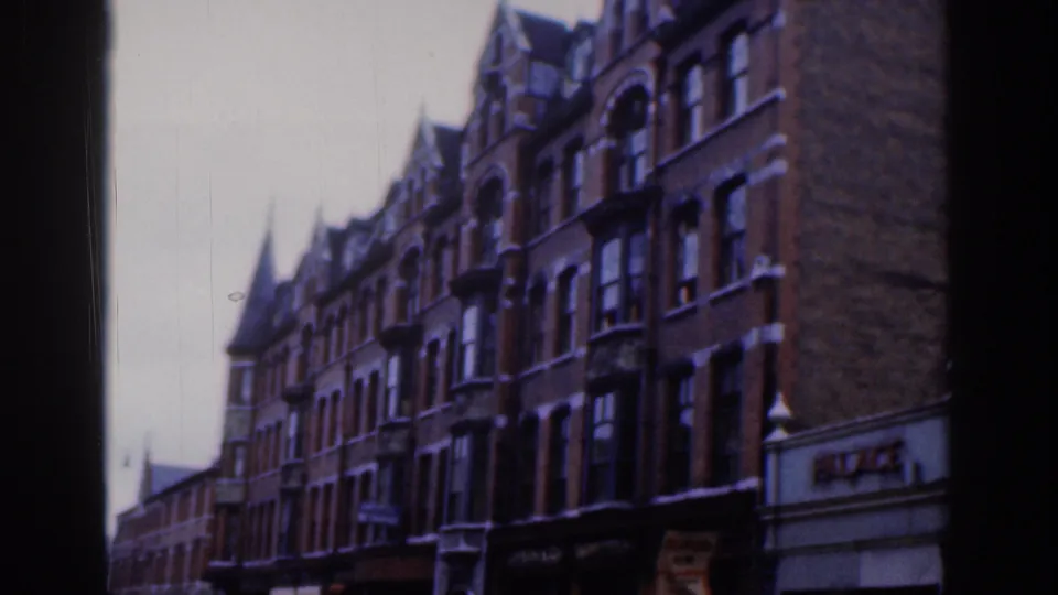 Handheld 8mm frame of Dublin buildings with bay windows, storefronts, decorative stonework, and the PALACE sign near the right edge.
