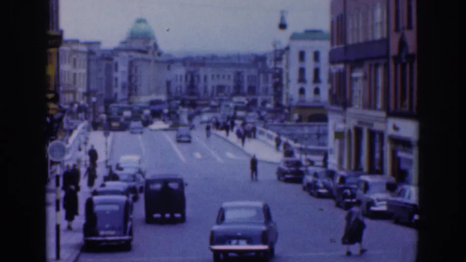 1961 Dublin view looking down a busy street toward a domed building, with cars, a van, pedestrians, and commercial facades visible.
