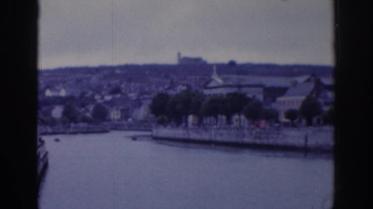 1961 Dublin home-movie view across a river or basin toward trees, waterfront buildings, and a distant hillside.