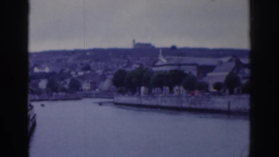1961 Dublin home-movie view across a river or basin toward trees, waterfront buildings, and a distant hillside.