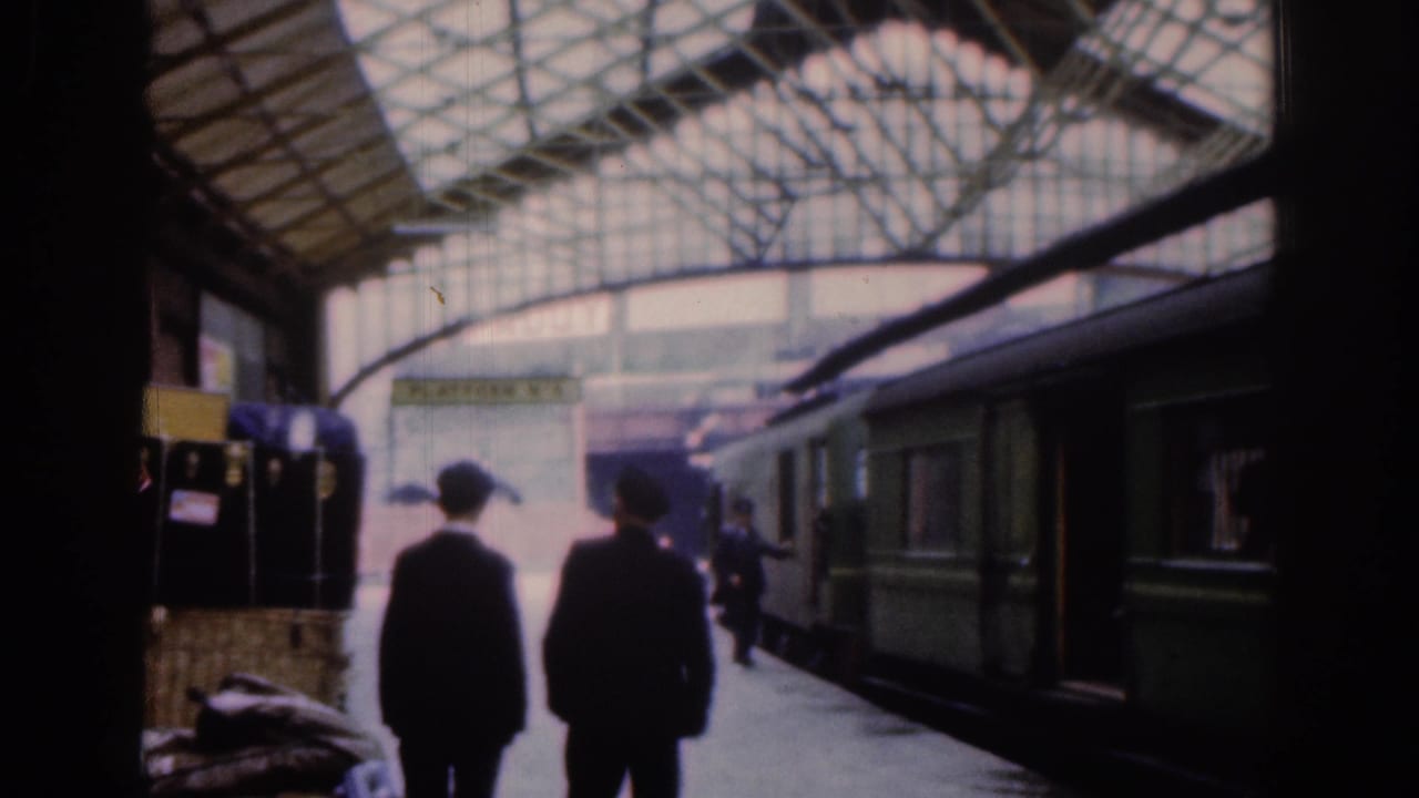 Two dark-clad passengers move along the Dublin station platform in 1961 as a green passenger train stands alongside the arched glass-and-steel roof.