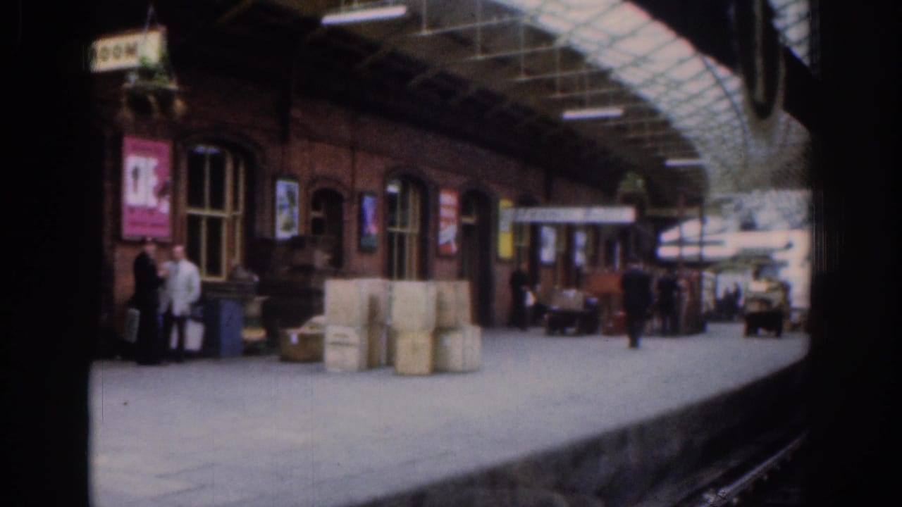 Brick station building with posters, stacked crates and passengers on the platform.