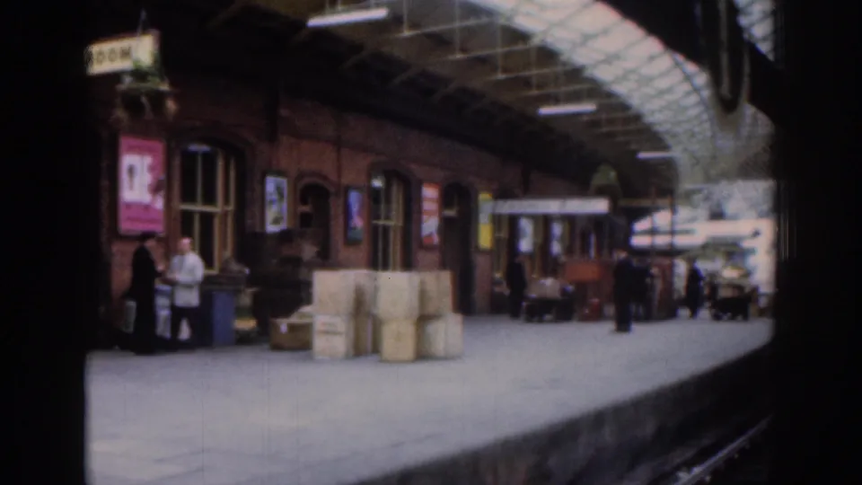 1961 Dublin platform detail with stacked crates, poster boards, a brick station wall and passengers under the roof canopy.