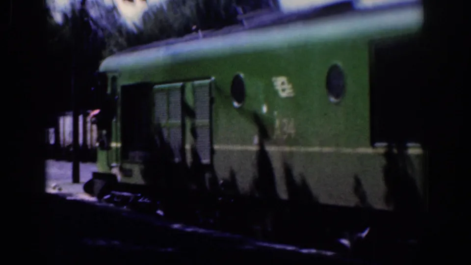 Close side view of a green railway carriage in the Dublin 1961 clip, with circular windows and partially visible rail markings.