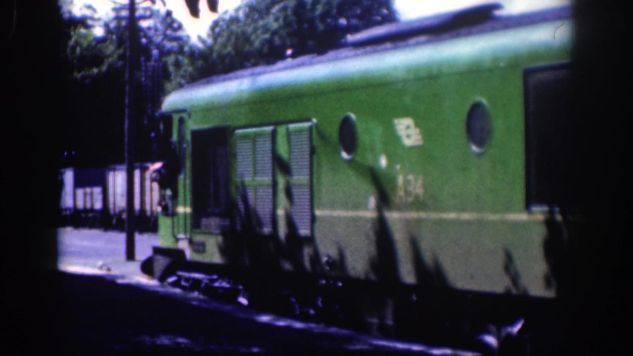 Green rail car with round windows and side markings near a platform.