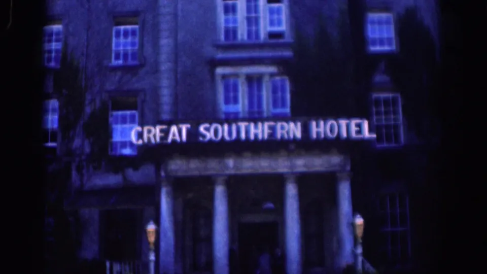 1961 Dublin home-movie frame of the Great Southern Hotel at night, showing the illuminated sign, facade windows, and columned entrance.
