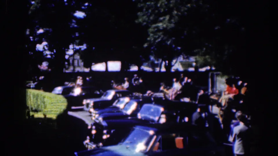 1961 Dublin frame with parked cars in the foreground, pedestrians along the curb, and part of a horse-drawn carriage at right.