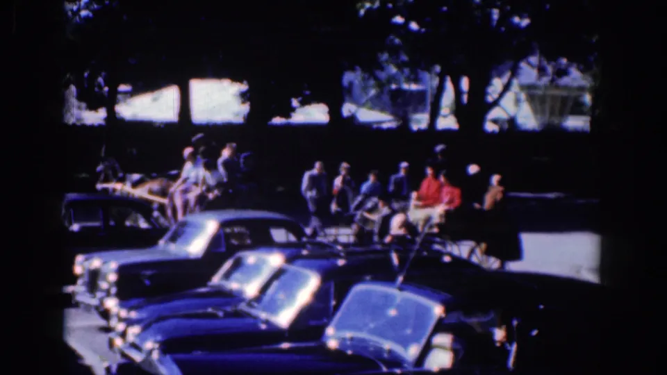 1961 Dublin home-movie still with horse, buggy, pedestrians, and blue-toned parked cars along a shaded street.