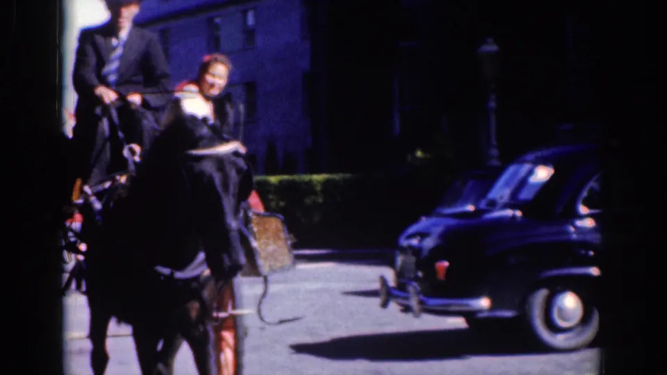 1961 Dublin frame showing a horse-drawn carriage and a rounded dark car sharing a bright urban street.