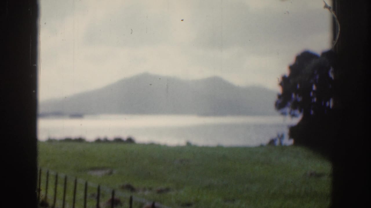Soft lakeside view with mountains, grass, overcast sky, and dark frame edges.
