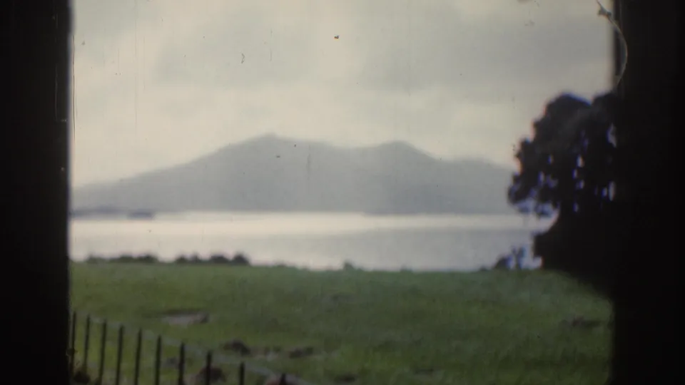 1961 Ireland 8mm view across a grassy lakeshore toward muted mountains under an overcast sky.