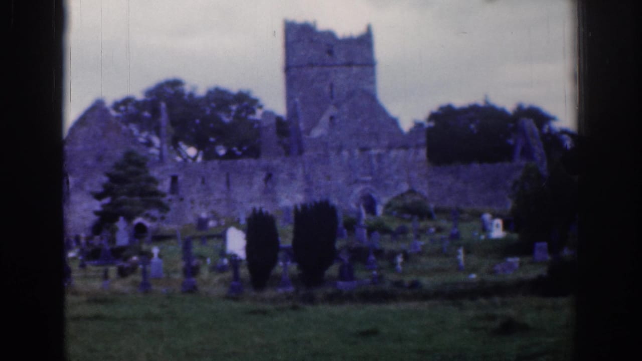 1961 Dublin home-movie frame showing a stone church ruin behind a grassy cemetery with scattered gravestones and trees.