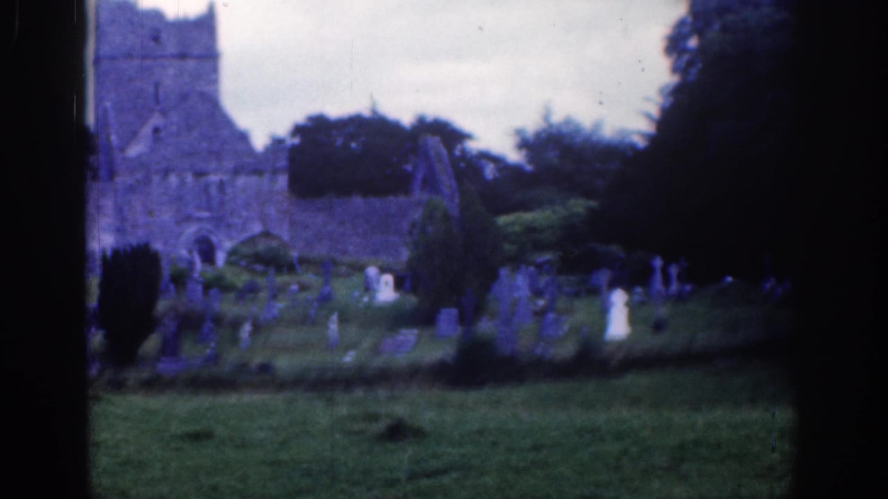 1961 Dublin home-movie frame showing a stone ruin and graveyard with weathered markers in soft, blue-shifted 8mm color.