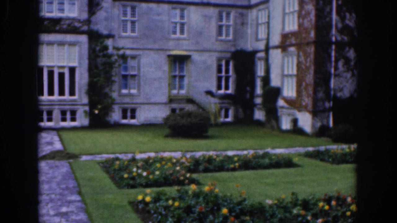 Formal garden and stone mansion with flowerbeds, lawn, path, and dark foreground frame.