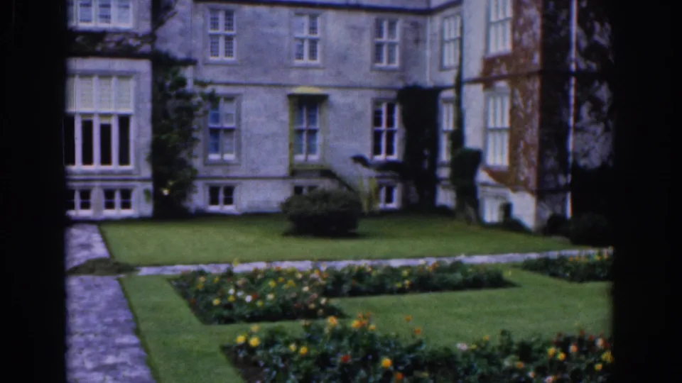 Dublin estate garden in 1961 with a stone mansion facade, neat flowerbeds, clipped lawn, and a dark window-like border.