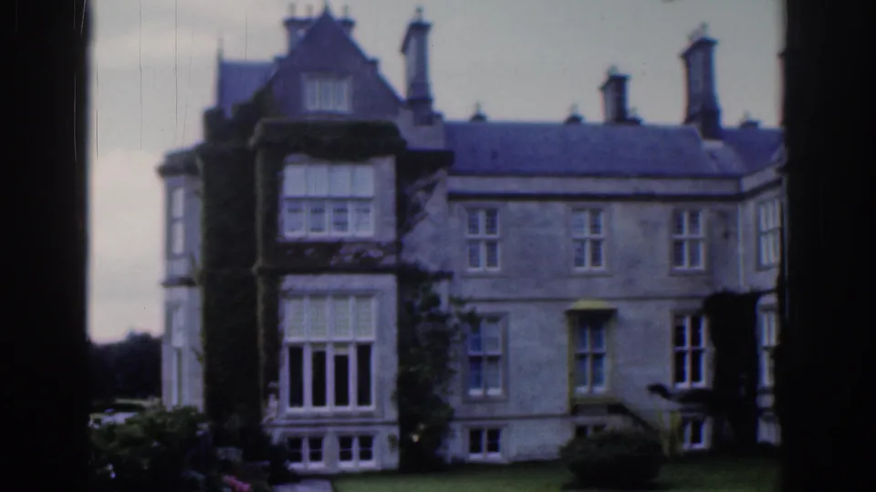 1961 Dublin frame of the same stone manor exterior, showing ivy growth, chimneys, window bays, and garden lawn.