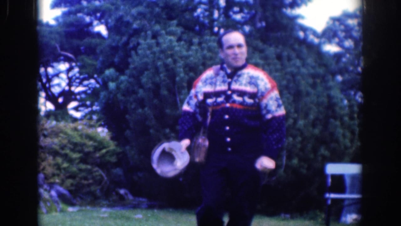 In 1961 Dublin home-movie footage, a man in a colorful sweater stands in a park holding a light-colored hat.