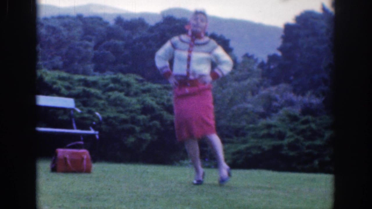Woman stands mid-step on the lawn, hands at her hips, with trees behind her.