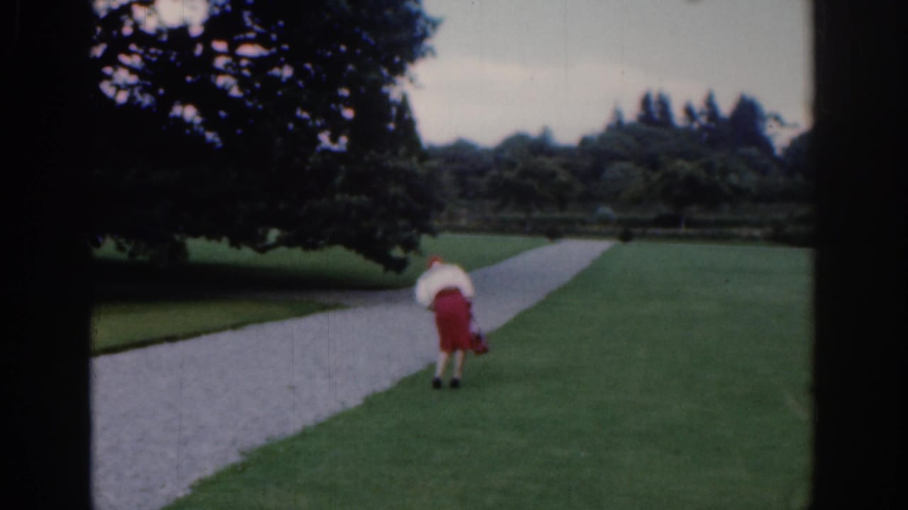 Woman bends slightly while walking on a park lawn near a gravel path and trees.